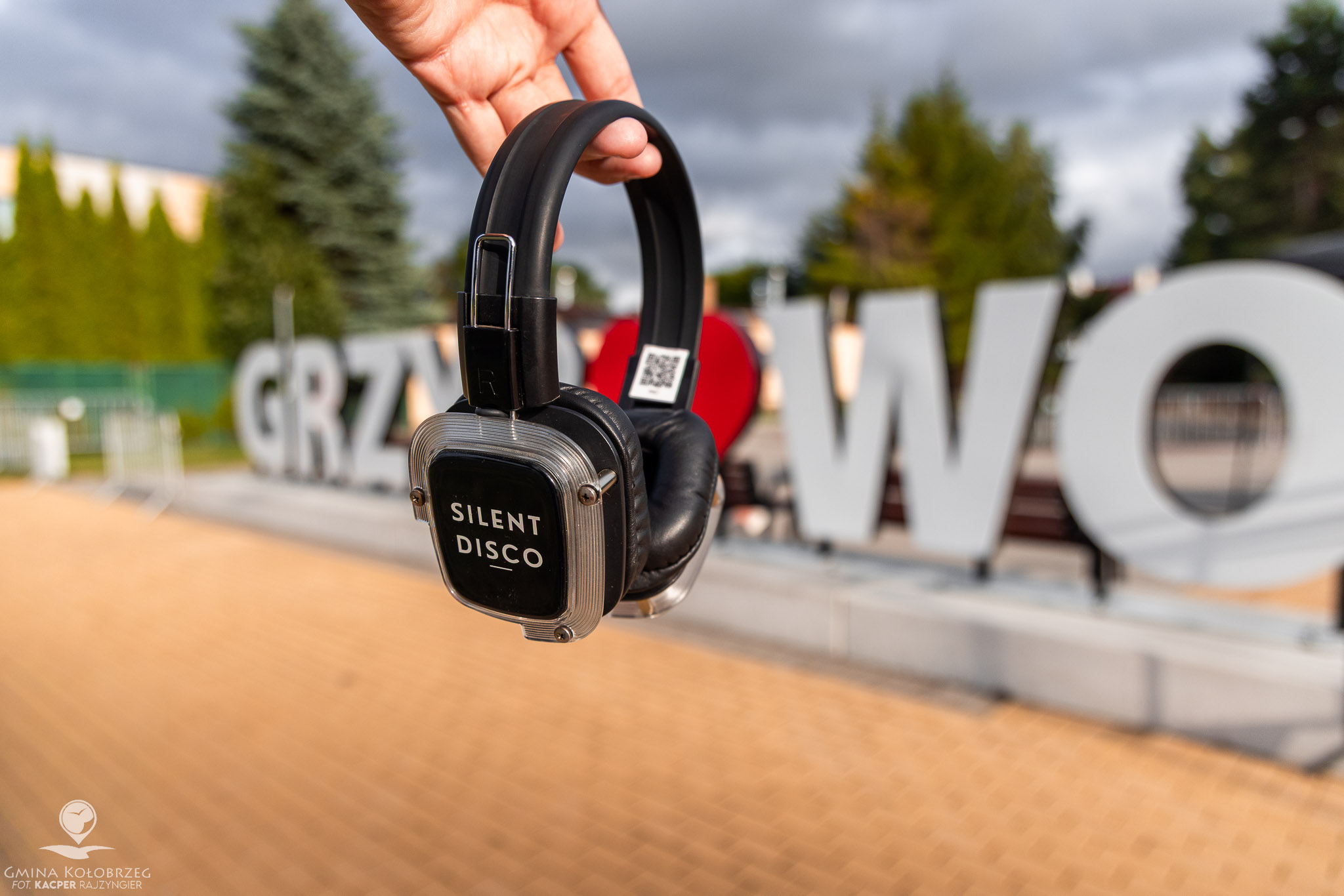 Zdjęcie przedstawia słuchawki z napisem &bdquo;Silent Disco&rdquo; trzymane na tle napisu &bdquo;Grzybowo&rdquo;. Ujęcie nawiązuje do plenerowego wydarzenia muzycznego, z rozmytym tłem i ciepłym światłem.